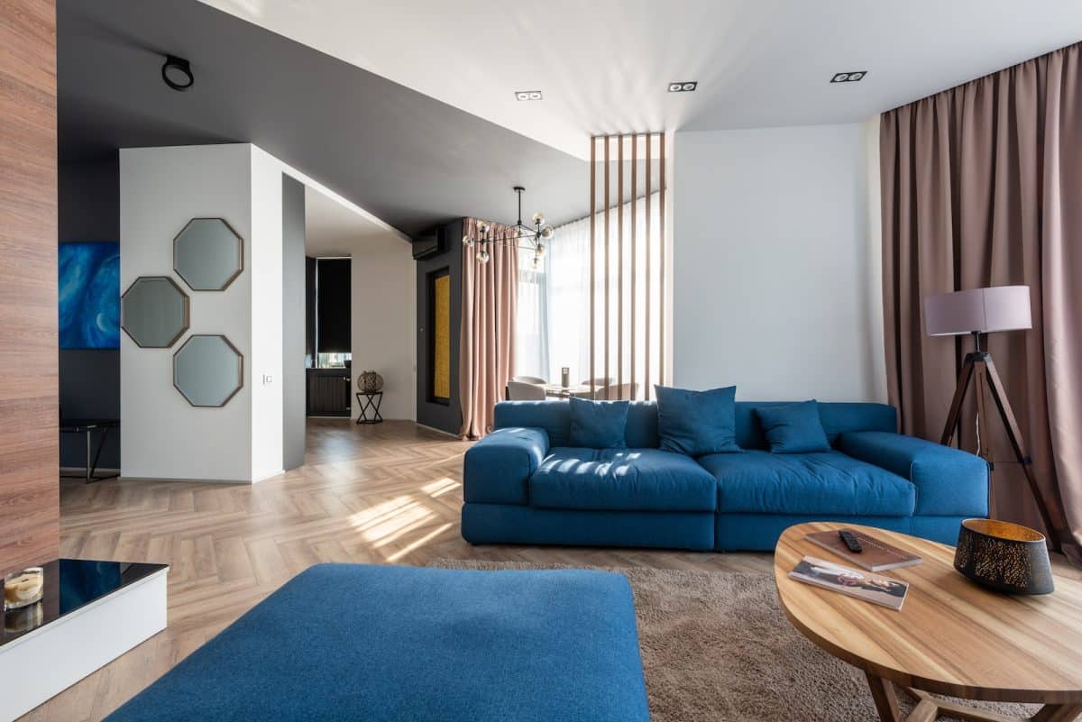 Interior of spacious flat with blue sofa and pouf near wooden table placed on carpet near wall with stylish decorations