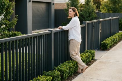 Femme appuyée sur une clôture aluminium anthracite sur mesure devant un jardin soigné avec portail assorti