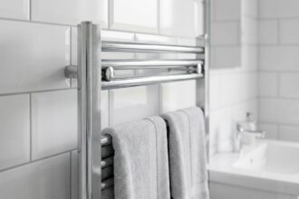 Sèche-serviettes chromé moderne monté sur un mur carrelé blanc dans une salle de bain contemporaine avec serviettes grises