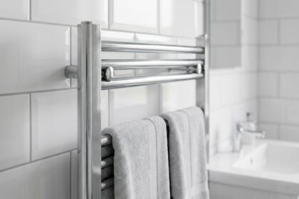 Sèche-serviettes chromé moderne monté sur un mur carrelé blanc dans une salle de bain contemporaine avec serviettes grises